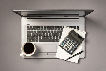 Top view photo of cup of drink calculator pen and notebook on grey laptop on isolated grey...