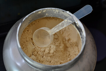 An empty spoon in a big whey protein powder grey can