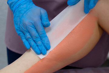 Obraz premium The stage of the epilation procedure.Removal of unwanted hair on the legs.The master removes the wax with the help of special bandage strips for depilation.Orange wax is applied to the legs.