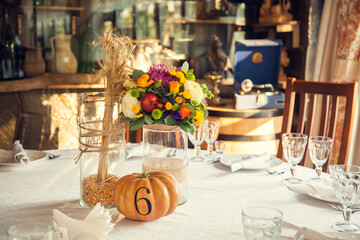Festive floristry in autumn style with numbering of tables on pumpkins in banquet hall.