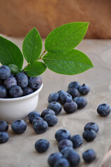 Freshly picked blueberries in a white bowl. Juicy and fresh blueberries with green leaves. Antioxidant. Healthy food concept. Healthy organic seasonal fruits background.