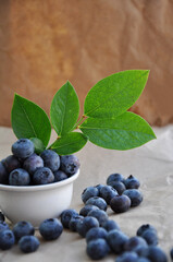 Freshly picked blueberries in a white bowl. Juicy and fresh blueberries with green leaves. Antioxidant. Healthy food concept. Healthy organic seasonal fruits background.
