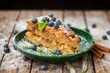 Piece of tasty pie with blueberries on wooden table, cinnamon and mint