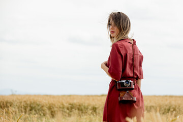 young woman in red dress with camera on wheat field