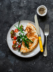 Oatmeal pancake without flour with asparagus, feta and cherry tomatoes - a delicious diet breakfast on a dark background, top view