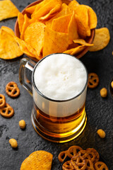 Beer with snacks on rustic background. Pretzels, nuts and corn chips