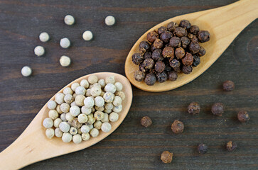 Top View of Spoons of White Peppercorns and Black Peppercorns on Black Wooden Background
