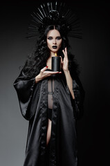 Halloween theme: dangerous young witch dressed in black cloak and headwear with roses and spikes....