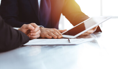 Business people using tablet computer while working together in sunny modern office. Unknown businessman with colleague at workplace. Teamwork and partnership concept