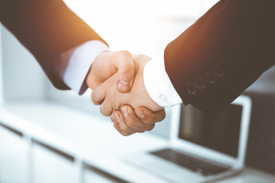 Businessman and woman shaking hands in sunny office, close-up. Concept of handshake as success symbol in business