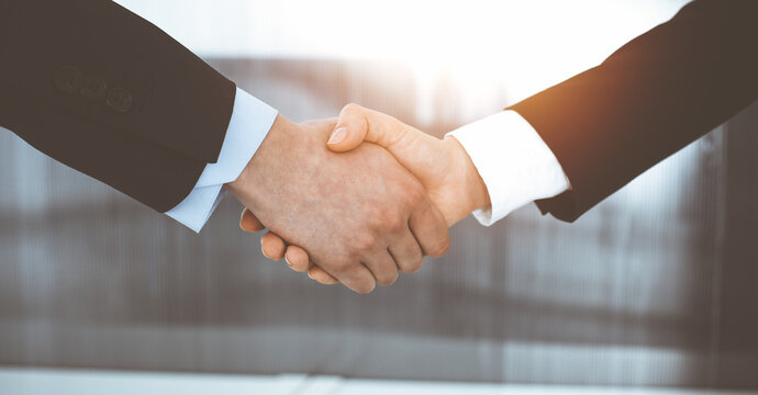 Businessman and woman shaking hands in sunny office, close-up. Concept of handshake as success symbol in business
