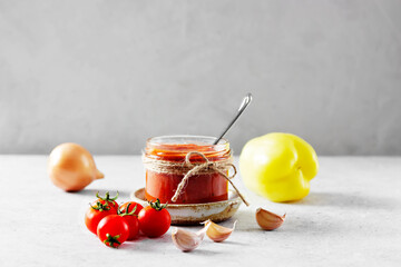 Authentic Spanish Sofrito sauce made with tomato, peppers, onion, garlic, herbs and olive oil in glass jar. Concrete background, side view