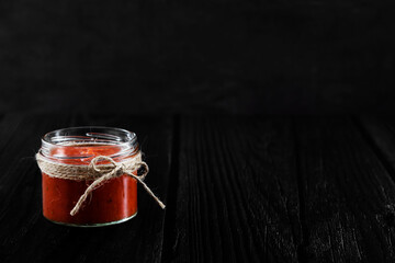 Authentic Spanish Sofrito sauce made with tomato, peppers, onion, garlic, herbs and olive oil in glass jar. Dark wooden background, side view with copy space