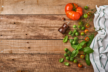 Fresh cherry tomato branches, basil leaves, napkin, pepper and pepper mill on old wooden rustic background. Food cooking background and mock up.