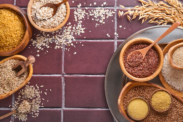 White, brown and red rice, buckwheat, millet, corn groats, quinoa and bulgur in wooden bowls on a brown stone kitchen table. Gluten-free cereals. Top view with copyspace