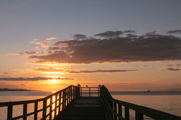 Silhouette of a romantic pier at sunrise as sea holidays concept