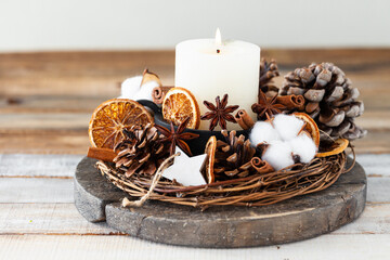 Rustic decor for christmas holiday family dinner. Center piece with white candle, dry orange, cones, cotton. Zero waste eco friendly home decoration. Cozy atmosphere, wooden background. Close up