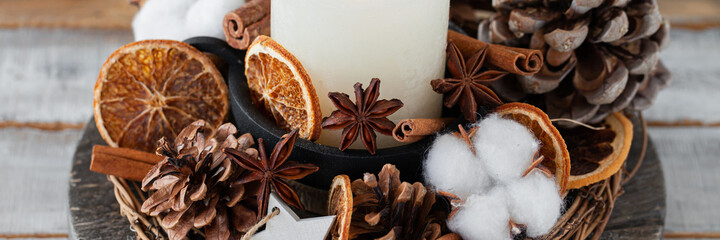 Rustic decor for christmas family dinner. Center piece with white candle, dry orange, cone, cotton. Zero waste eco-friendly home decoration. Cozy atmosphere, wooden background. Close up banner
