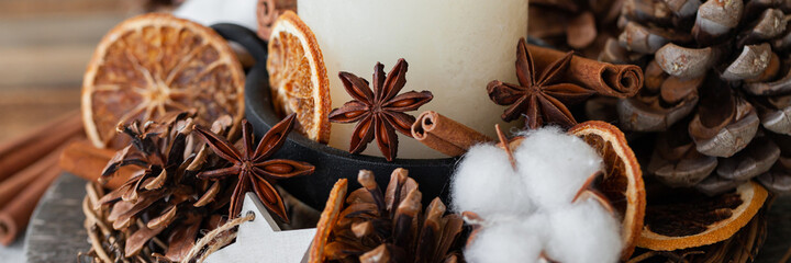 Rustic decor for christmas family dinner. Center piece with white candle, dry orange, cone, cotton. Zero waste eco-friendly home decoration. Cozy atmosphere, wooden background. Close up banner