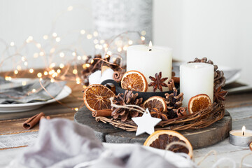 Rustic decor for christmas holiday family dinner. Center piece with white candle, dry orange, cones, cotton. Zero waste eco friendly home decoration. Cozy atmosphere, wooden background. Close up