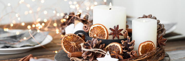 Rustic decor for christmas family dinner. Center piece with white candle, dry orange, cone, cotton....