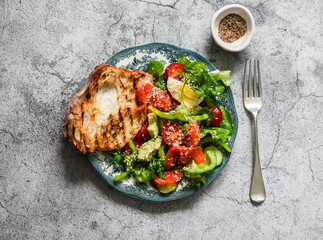 Delicious salad for breakfast, snack - salad with salmon, egg, vegetables, lettuce and grilled bread on a grey background, top view