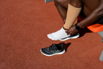 A black male track and field athlete puts compression leggings on his leg before a race at the...