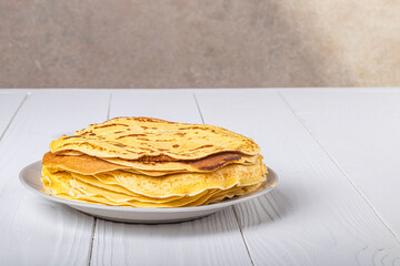 white wooden background in retro style. the plate in it is thin yellow pancakes. close-up.