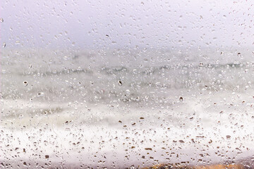 Window with raindrops and storming sea behind. Rainy weather. Water drops on the glass