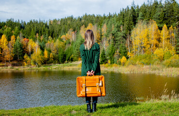 woman in cloak with suitcase near lake and forest in autumn season