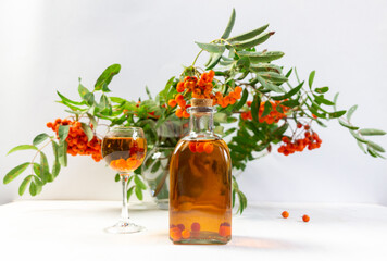 rowan berry tincture in glass and bottle with rowanberry branhes bouquet in vase on white background © Natalya