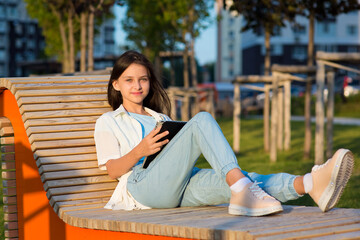 a smiling girl is sitting on a bench on the street and holding a tablet in her hands