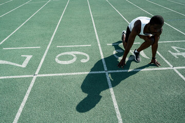An African American male track and field athlete in sportswear stands at a low start before the race at the stadium