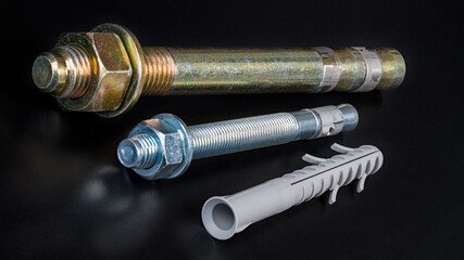 Galvanized wedge expansion anchor bolts and plastic split-ribbed dowel on a black background....
