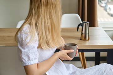 Girl drinks delicious black coffee prepared in a moka pot coffee maker. Morning drink for breakfast. Fragrant black coffee in a cup close-up. Equipment for making coffee