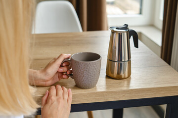 Girl drinks delicious black coffee prepared in a moka pot coffee maker. Professional coffee brewing. Morning drink for breakfast. Fragrant black coffee in a cup close-up. Equipment for making coffee