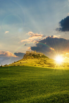 castle on the hill beneath a rainbow at sunset. composite fantasy landscape. grassy meadow in the foreground. rocky peaks of the ridge in the distant background in evening light