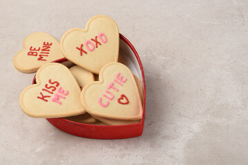A heart shaped box overflowing with heart shapes sugar cookies with different sentiments written in icing. - Powered by Adobe