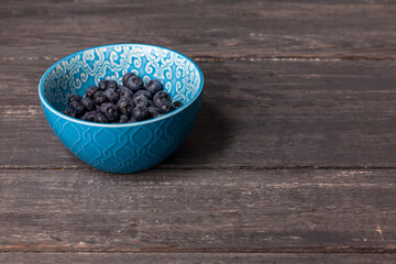 Blueberries in blue bowl on dark grey wooden background with copy space.