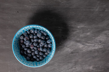 Blueberries in blue bowl on dark grey background. Flatlay.