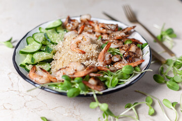 Quinoa with grilled prawns or shrimps, cucumber and micro greens on the marble background side view.