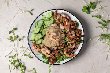 Healthy quinoa with grilled prawns or shrimps, cucumber and micro greens on the marble background.