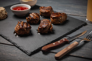Grilled pork medallions with ketchup served on stone board on dark wooden table.
