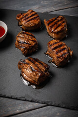 Grilled pork medallions with ketchup served on stone board on dark wooden table. Vertical orientation