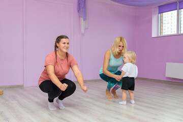 Fototapeta na wymiar Mom and baby are doing exercises with an instructor in the gym. Developmental exercises for the baby.