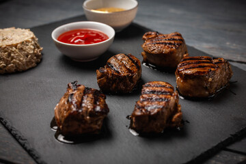 Grilled pork medallions with cheesy salad, ketchup and mustard on dark wooden table.