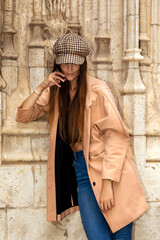 Girl in coat and hat looks down while talking on cell phone. Fashion and communication concept