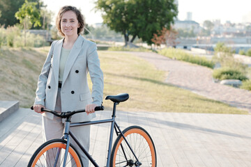Cute happy businesswoman with bicycle standing against park and riverside in the city