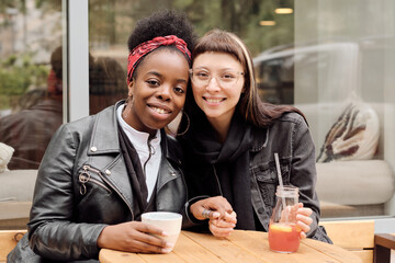 Young cheerful girlfriends in casualwear looking at you with toothy smiles in outdoor cafe