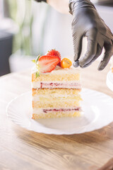 The girl decorates a piece of cake with fresh strawberries